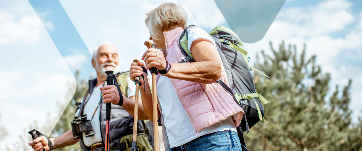 Two retirees hiking outdoors with trekking poles and backpacks, reflecting the financial confidence a workplace retirement savings plan can help build.